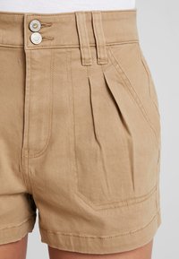 Khaki shorts made of lightweight fabric with a high waistband, two button closures, pleated front, and angled pockets.