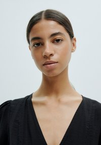 Schwarzes V-Ausschnitt-Oberteil mit kurzen Puffärmeln; weiche Textur; glattes Material; minimalistisches Design; getragen von einem Modell mit dunklem Haar.