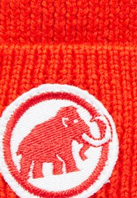 Cappello rosso lavorato a maglia con una toppa circolare bianca decorata con un disegno di elefante ricamato in rosso. Tessuto testurizzato con motivo a coste.