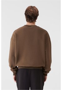 Sweatshirt marron supradimensionat, realizat dintr-un material moale, cu umeri căzuți, gât rotund și manșete cu nervuri la mâneci și margine.