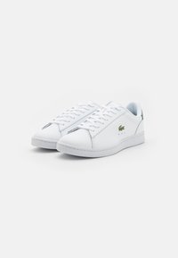 Sneakers bianchi in pelle con lacci piatti, punta arrotondata, dettaglio verde sul tallone e piccole perforazioni per la traspirabilità.