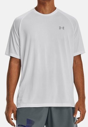 Mann trägt ein schlichtes weißes kurzärmeliges Sportshirt mit grauem Under Armour-Logo auf der Brust und graue Shorts mit marineblauem Grafikdesign.