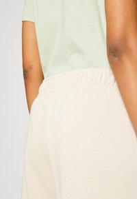 Beige sweatpants with an elastic waistband and side pockets, paired with a light green t-shirt, showcasing soft, smooth fabric textures.