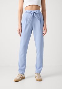 Lyseblå bukser med høj talje og bælte, lavet af et glat materiale og i slim fit, suppleret med en sidelomme. Båret med beige sneakers.