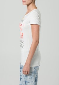 Hvid bomulds t-shirt med korte ærmer, har rødt og sort trykt tekstdesign. Parret med en lys blå tie-dye nederdel.