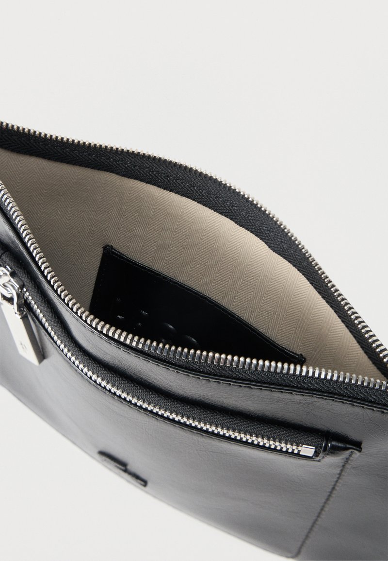 Borsetta in pelle nera con cerniera, fodera interna in tessuto beige e tasca interna, mostrata aperta su uno sfondo chiaro.