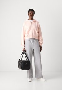 Felpa rosa chiaro con zip, pantaloni grigi con vita elastica, sneaker bianche e una borsa nera in pelle con dettaglio a cerchio. Texture morbide e vestibilità casual.