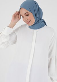 White shirt with a button placket, long puff sleeves, and a smooth texture. Paired with a solid blue hijab, soft fabric.