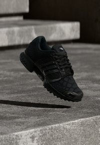 Scarpa sportiva nera con tomaia testurizzata, caratterizzata da un design con lacci e accenti lisci a contrasto. Suola leggera e forma aerodinamica.