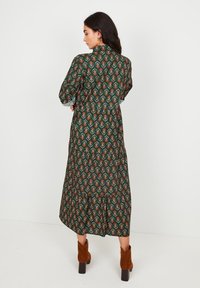 Femme de profil portant une longue robe florale vert foncé à manches longues et des bottes en daim marron à la cheville.