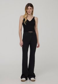 Top corto nero a costine con scollatura a V e design aderente, abbinato a jeans neri a zampa. Il modello indossa anche sneakers bianche con suola color beige.