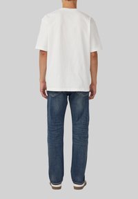 Biała koszulka z krótkim rękawem i okrągłym dekoltem, w zestawie z niebieskimi dżinsami z tylnymi kieszeniami i dopasowanym krojem.