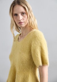 Suéter amarillo, esponjoso de punto con un escote amplio y mangas cortas abullonadas. Textura suave, corte holgado y material de punto ligero.