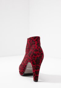 Bottine en daim rouge avec un motif léopard, talon aiguille fin et texture lisse. Bout arrondi avec un design haute coupe.