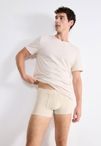 Boxer-briefs beiges en tissu doux, avec une coupe ajustée et une ceinture élastique, associés à une chemise à manches courtes beiges assortie.