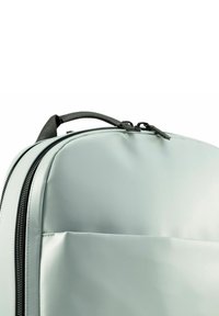 Hellgrauer Rucksack mit glatter, strukturierten Oberfläche, ausgestattet mit einer Fronttasche, doppelt zipbaren Reißverschlüssen und einem schwarzen Tragegriff für einfachen Transport.