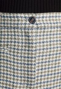 Geweven houndstooth broek met groene, blauwe en beige patronen, voorzien van een bruine knop en elastische tailleband.