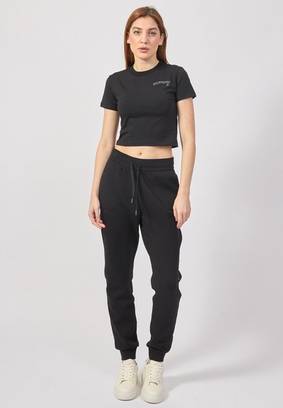 T-shirt nera cropped con maniche corte, dotata di un piccolo logo. Abbinata a pantaloni della tuta neri e sneakers beige. Design semplice, vestibilità casual.