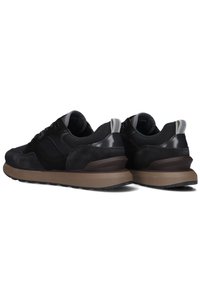 Zwarte sneakers met een bovenwerk van suède en mesh, voorzien van een dikke bruine rubberen zool. Reflecterende accenten op de achterkant en veters voor extra detail.