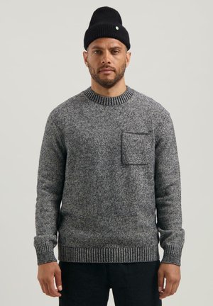 Grau strukturiertes Strickpullover mit Rundhalsausschnitt, gerippten Bündchen und einer Brusttasche, getragen mit einer schwarzen Mütze.