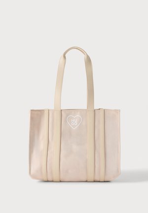 Beige boodschappentas met lange hengsels, verticale riemdetails en een hartlogo met "HUGO" gecentreerd aan de voorkant.