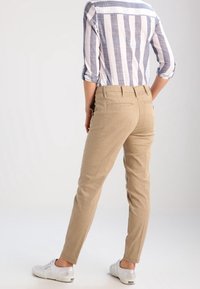 Beige puuvillachambray-housut, joissa on slim fit -malli, takataskut ja sinivalkoisen raidallisen paidan rullatut hihavat, yhdistettynä valkoisiin tennareihin.