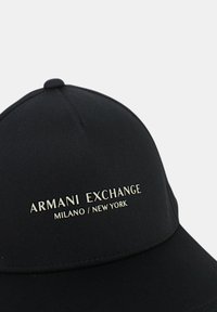 Cappello nero con design strutturato, con la scritta "ARMANI EXCHANGE MILANO / NEW YORK" in rilievo dorato sul pannello frontale.