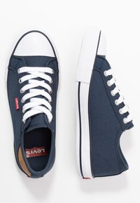 Navy canvasowe trampki Levi's mają białą gumową osłonę palców oraz podeszwę, białe sznurówki i metalowe oczka. Czerwone logo Levi's z boku.