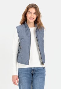 Leichter, grauer, gesteppter Weste mit einem Reißverschluss auf der Vorderseite, hohem Kragen und seitlichen Taschen, kombiniert mit einem weißen Sweatshirt und blauen Jeans.