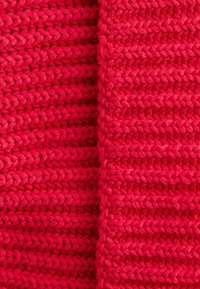 Knitted fabric in bright red, featuring a textured, chunky pattern with interlocking strands and a soft, smooth finish.