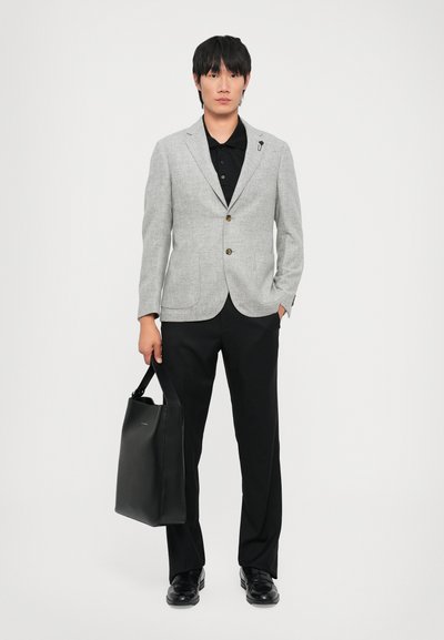 Gray blazer with brown buttons over a black shirt, paired with black trousers. Model holds a black leather tote bag.