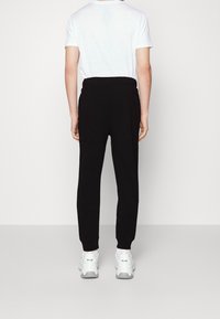 Black joggers with a high waistband, tapered legs, and ankle cuffs, paired with a plain white t-shirt and white sneakers.