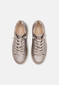 Graue Sneakers mit glatter, metallischer Oberfläche, ausgestattet mit einem Schnürdesign, beigen Schnürsenkeln und dezentem Branding auf der Innensohle.