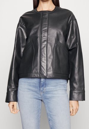 Frau trägt eine schwarze Lederjacke mit langen Ärmeln und zwei Vorderentaschen über hellblauen Jeans.