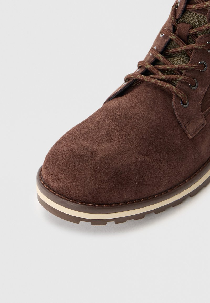 Stivale in suede marrone con punta arrotondata, colletto imbottito e suola bianca e marrone a contrasto con battistrada testurizzato per una presa migliore.