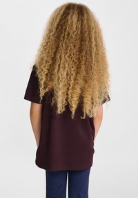 Czarnobordowa koszulka z krótkim rękawem, z okrągłym dekoltem i luźnym krojem. Na plecach widoczne długie, kręcone blond włosy.