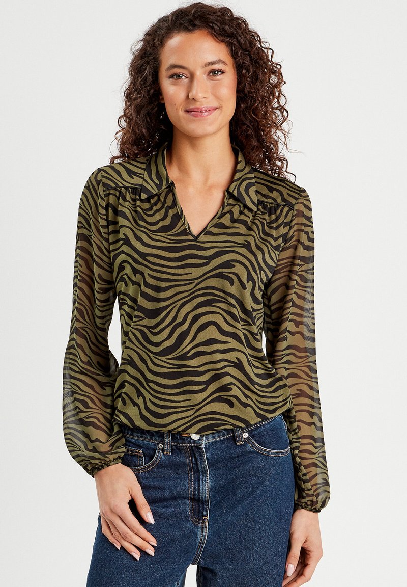 Blouse vert olive avec motif de rayures de tigre noires, présentant un décolleté en V, des manches longues transparentes et des détails froncés aux épaules.