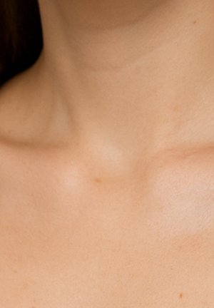 Gros plan sur la nuque et la clavicule, avec une peau lisse d'un ton légèrement hâlé et une texture naturelle subtile.