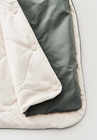 Wendbare Steppdecke mit cremiger Außenseite, die runde Knöpfe aufweist, und glattem dunkelgrauem Innenfutter auf weißem Hintergrund.