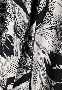 Tissu floral abstrait noir et blanc avec des motifs en points et en lignes, avec des boutons noirs sur un vêtement léger.
