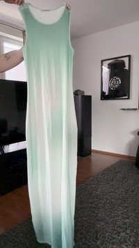 Ilga, be rankovių suknelė šviesiai žalia spalva, turinti gradientą nuo šviesesnių iki tamsesnių atspalvių, pagaminta iš lengvos, plaukuotų audinių.