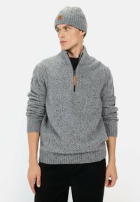 Grijze gebreide trui met een kwart-ritszak en geribbelde manchetten, gecombineerd met een bijpassende kabelgebreide beanie met een leren label.