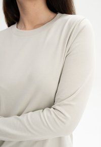 Hellgraues Langarmshirt aus weichem Baumwollstoff, mit Rundhalsausschnitt und gerippten Bündchen, sowie einer glatten Textur.