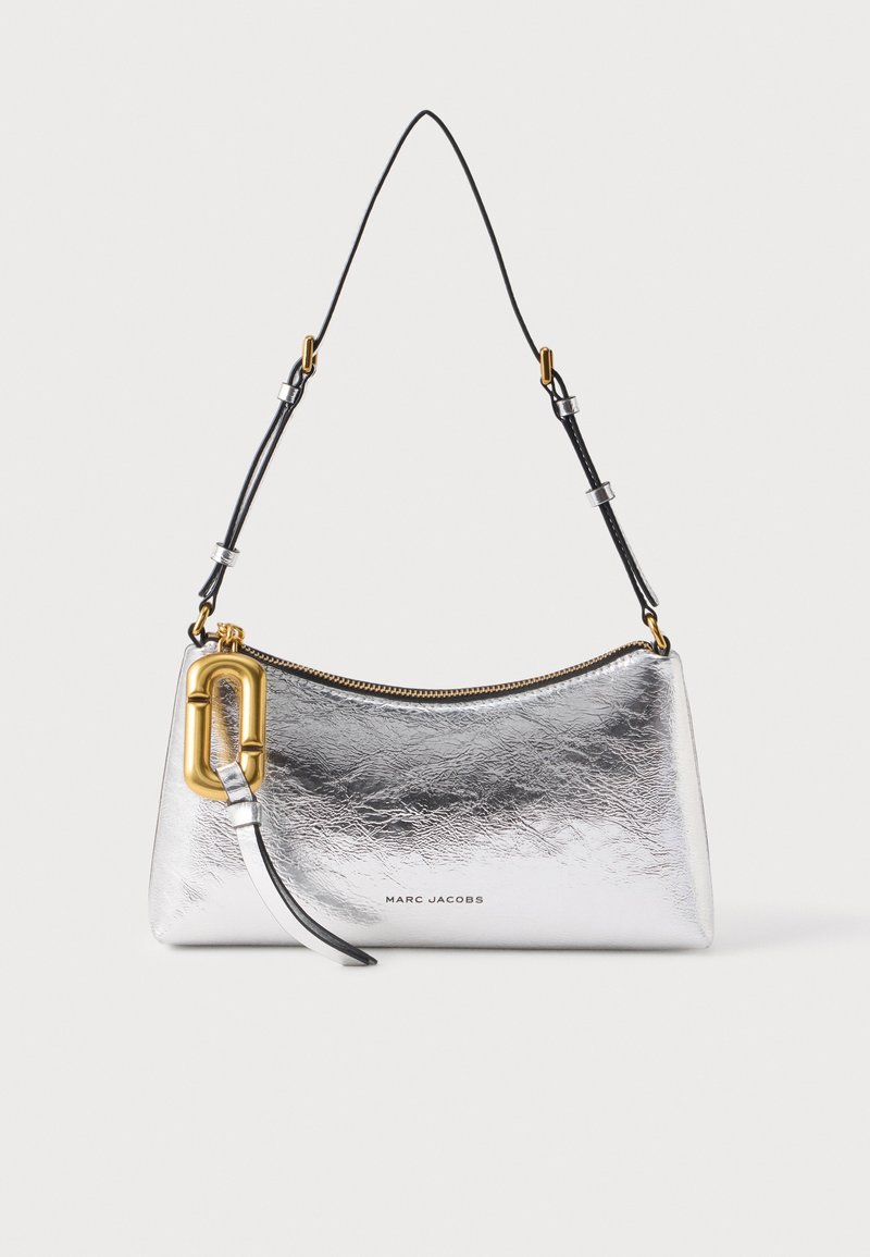 Sac à bandoulière métallisé argenté Marc Jacobs avec sangle noire réglable, fermeture éclair dorée et grande boucle décorative dorée sur fond blanc.