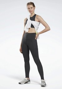 Fekete sportmelltartó íves varrásokkal és magas derekú leggings. Egy fehér, könnyű dzseki lazán rá van terítve. Elegáns ezüst futócipők.