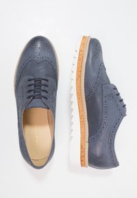 Scarpe in pelle di colore blu navy con design perforato, dettaglio wingtip, lacci e suola in gomma bianca con accenti in sughero.