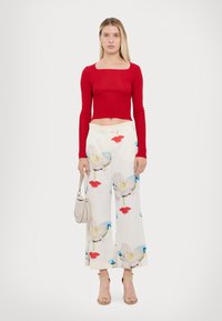 Un crop top rouge à rayures, à manches longues, associé à un pantalon large crème orné d'un imprimé floral en rose et bleu. Porte un petit sac à main gris.