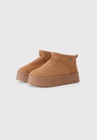 Bottines en suede marron avec une semelle compensée, un col rembourré et des détails de couture subtils. Design sans lacets avec une boucle au talon.
