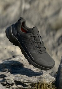 Scarpa sportiva nera con una tomaia testurizzata, punta rinforzata e suola resistente. Presenta lacci e tre strisce laterali. Design leggero.