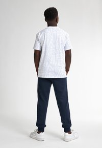 Camiseta blanca con un patrón audaz y contorneado, combinada con pantalones de chándal azul marino, con puños elásticos y zapatillas blancas.